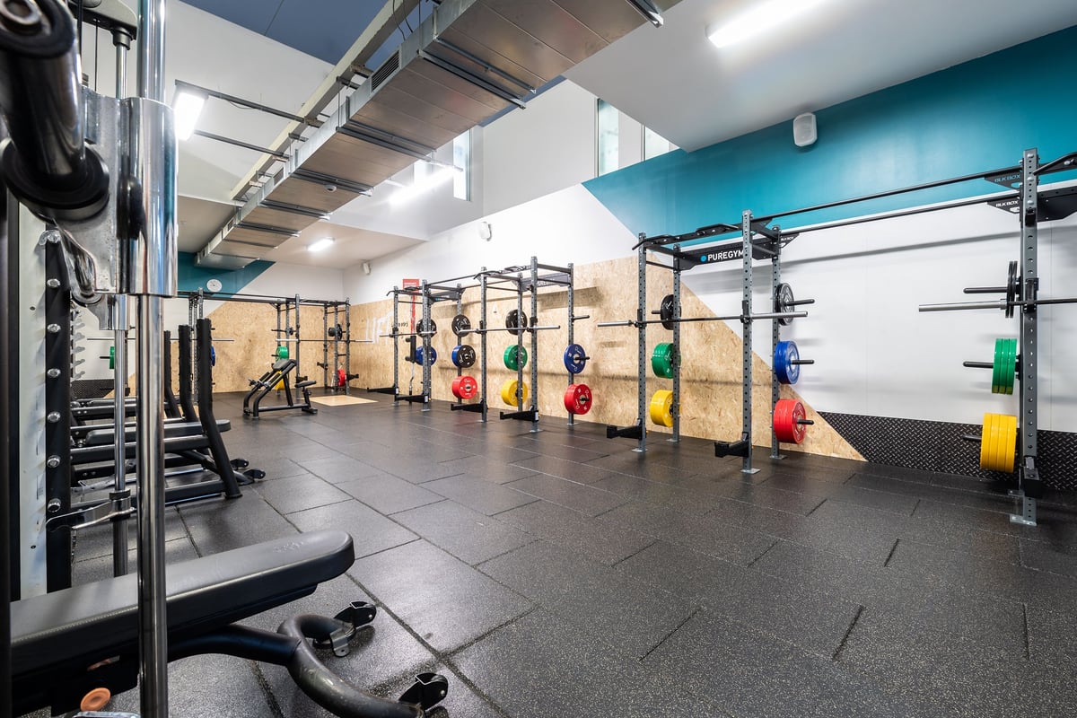 PureGym Sutton Coldfield: Squat racks, weight plates in multiple colours, barbells, and rubberized flooring in a gym.