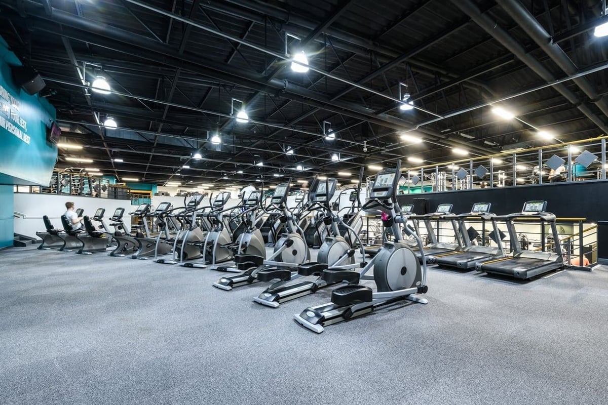 PureGym Portsmouth Commercial Road: Rows of elliptical machines and treadmills on rubberised flooring under bright lights.