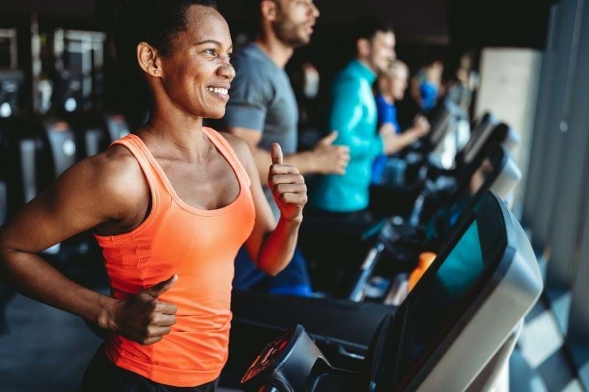 People running on treadmills in a gym with a woman in an orange top in the foreground