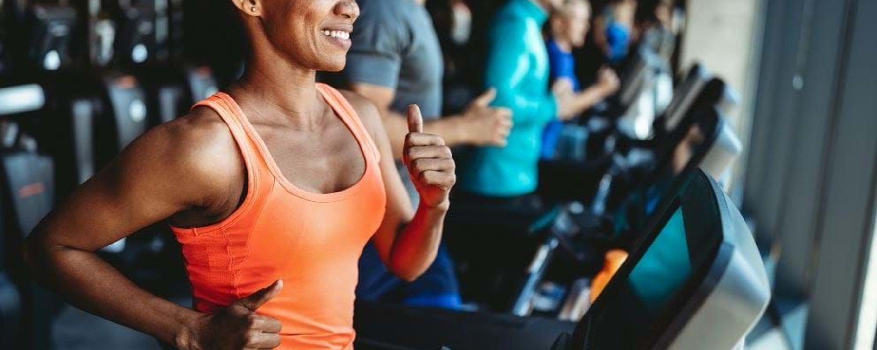 People running on treadmills in a gym with a woman in an orange top in the foreground