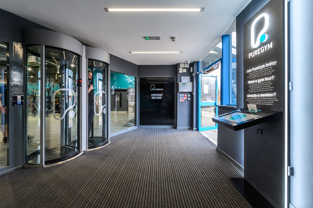 PureGym Bromborough: Rows of vending-style fitness equipment, glass walls, and directional signage.