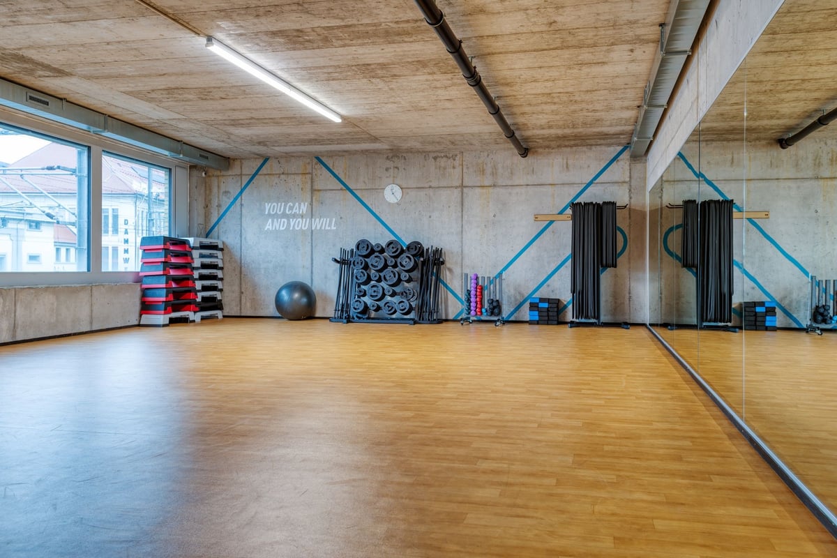 PureGym Lenzburg : espace d'entraînement fonctionnel avec poutres de plafond en bois, haltères et appareils
