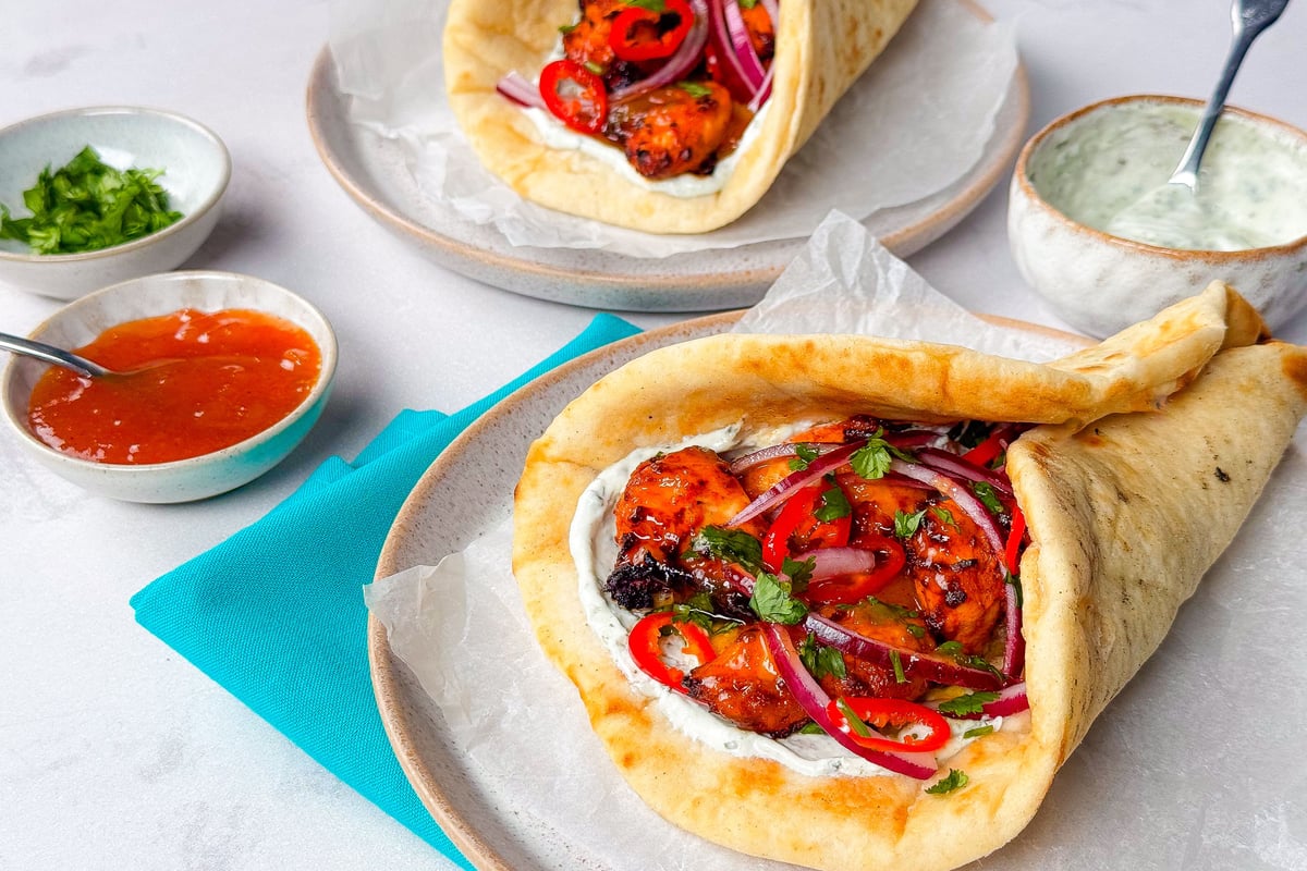 Two chicken wraps with red onions, chillies, and sauce on plates with dips nearby