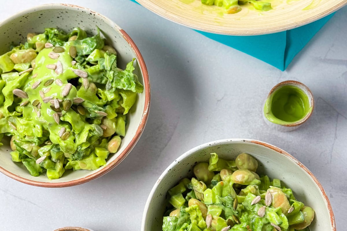 Green salad with beans and seeds in bowls on a light surface with a blue cloth