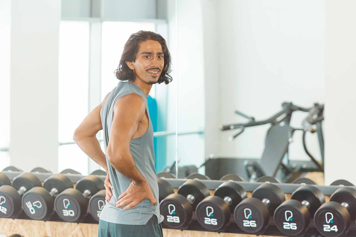 PureGym: male visitor wearing a vest posing in front of a row of dumbells