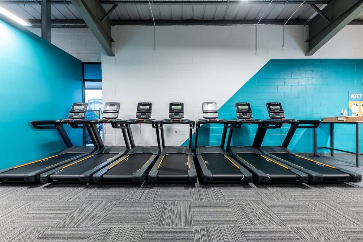 PureGym Alloa: Rows of treadmills with digital displays inside a bright teal and white fitness studio.