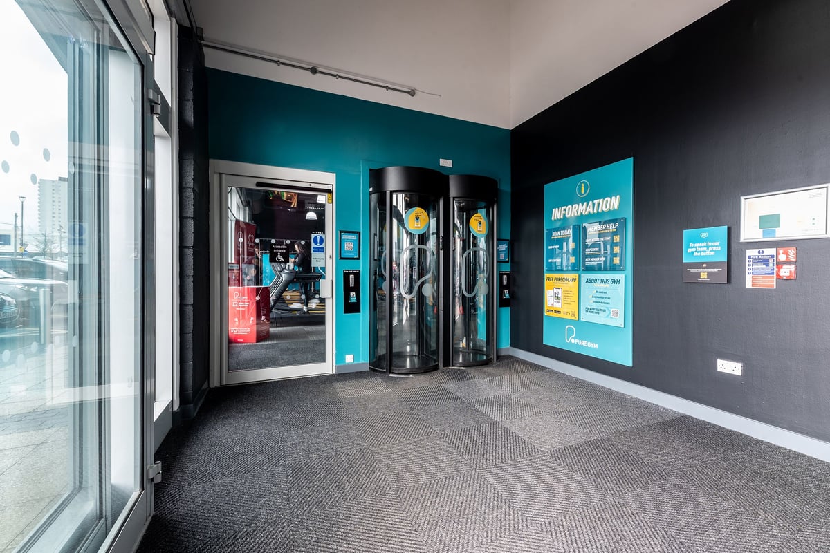 PureGym Wolverhampton Bentley Bridge: Glass entrance with turnstiles, vending machines, and gym information displays.
