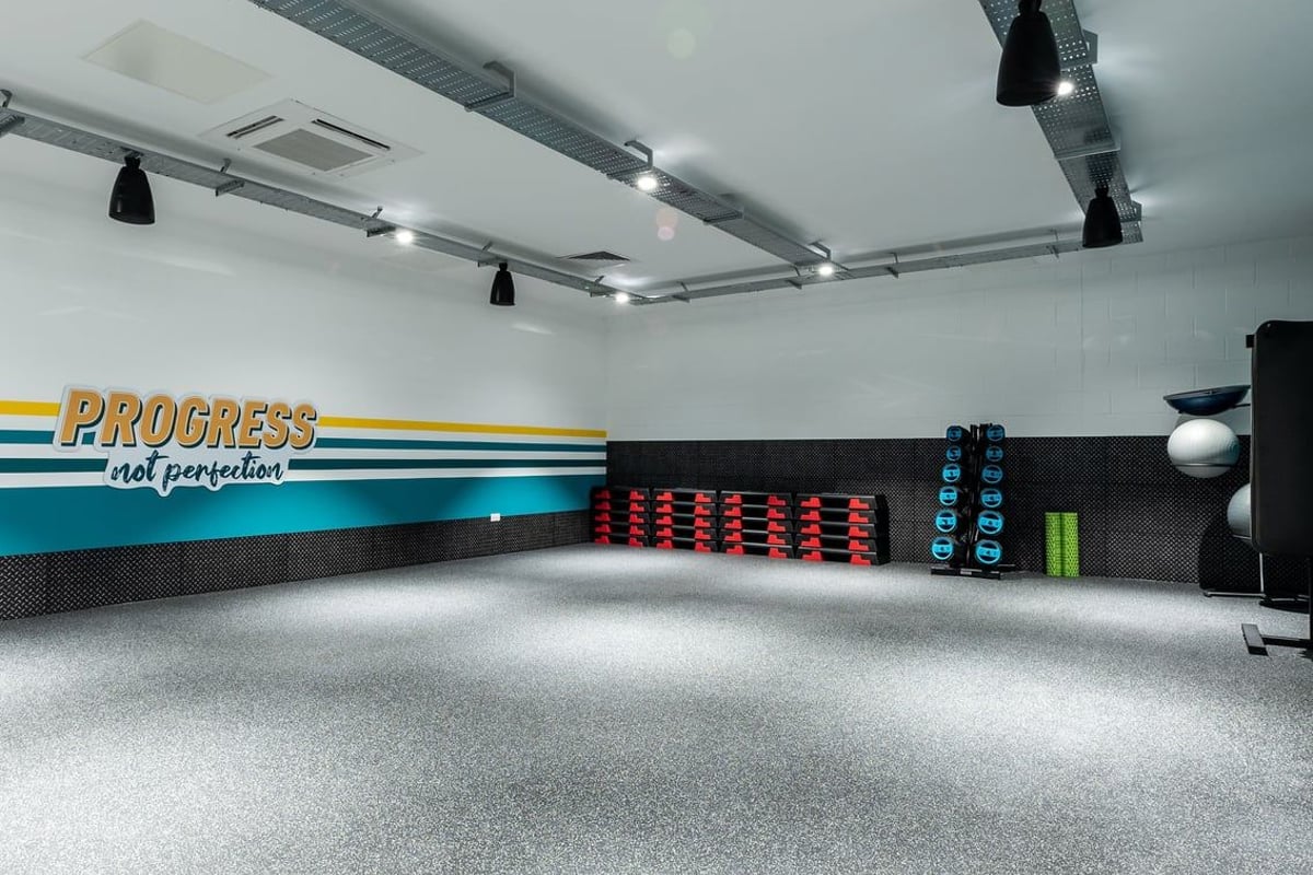 PureGym Alloa: Workout studio with weight plate rack, Progress branding, spotlights, and rubberized flooring.