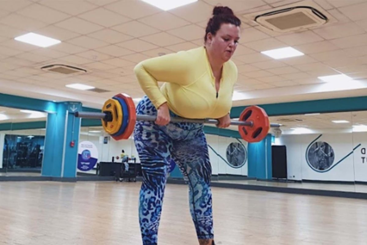 Frau hebt Langhantel im Fitnessstudio mit Spiegeln und Holzboden