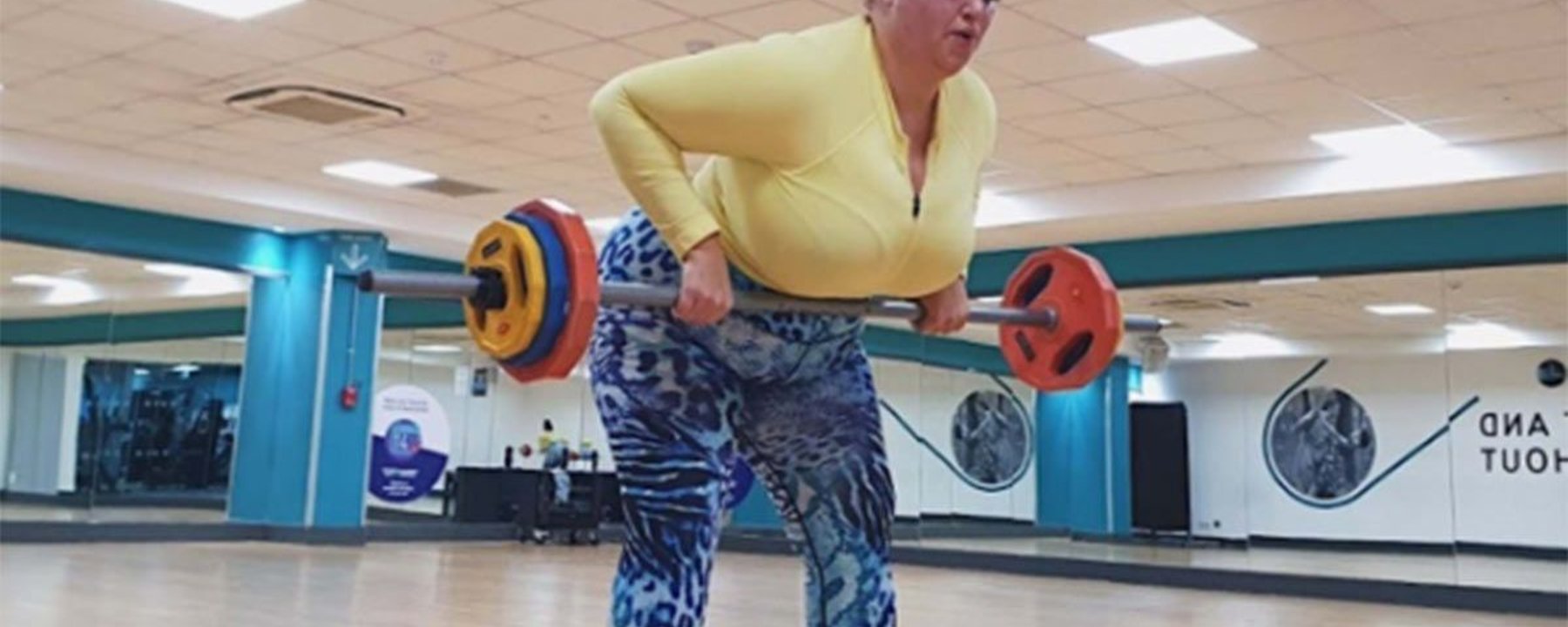 Frau hebt Langhantel im Fitnessstudio mit Spiegeln und Holzboden
