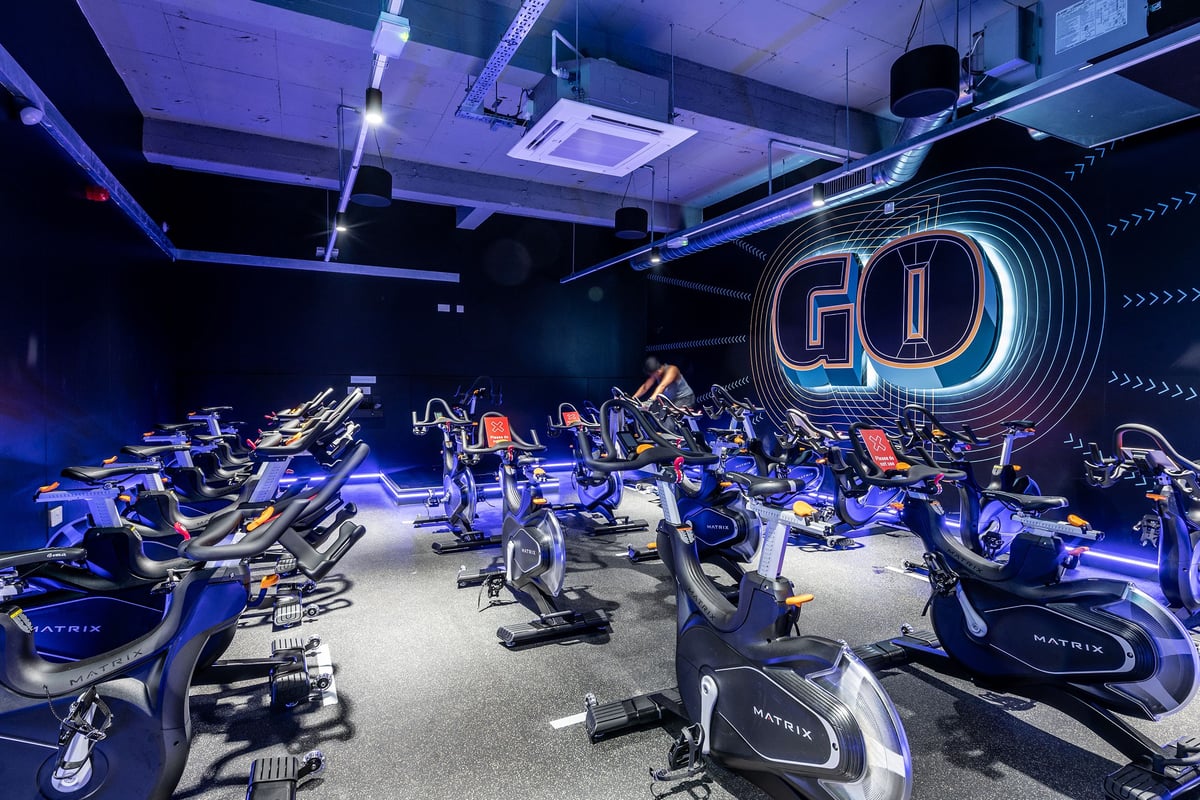 PureGym London Sydenham: Rows of stationary bikes with neon 'GO' signage in a dimly-lit studio.