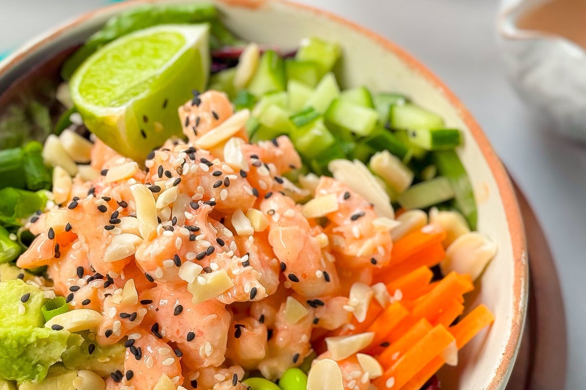 Bowl of poke with diced salmon, edamame, avocado, cucumber, carrot, lime, and sesame seeds