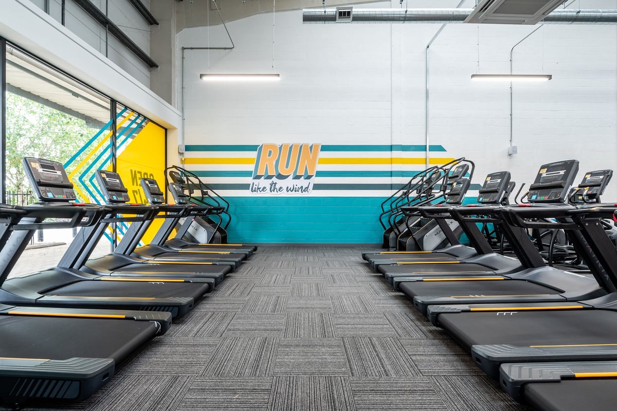 PureGym Thamesmead: Rows of treadmills in a colourful gym with motivational wall graphics.