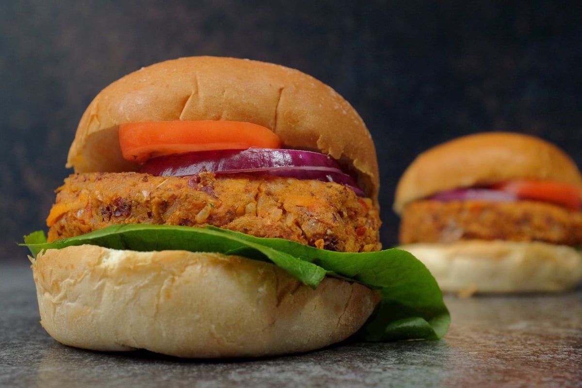 Veggie bean burger in a bun with lettuce, red onion and carrot on a grey surface