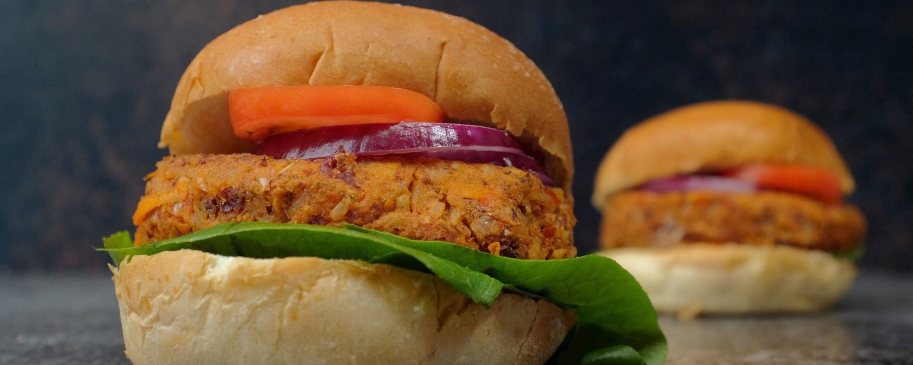 Veggie bean burger in a bun with lettuce, red onion and carrot on a grey surface