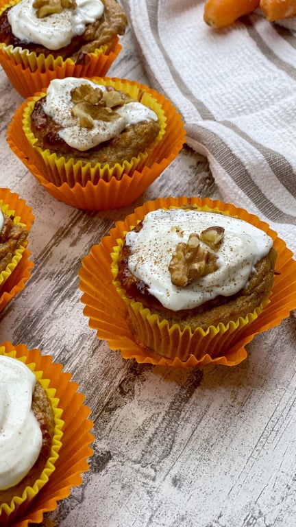 Carrot cupcakes with cream cheese frosting and walnut halves in orange cases on wood table