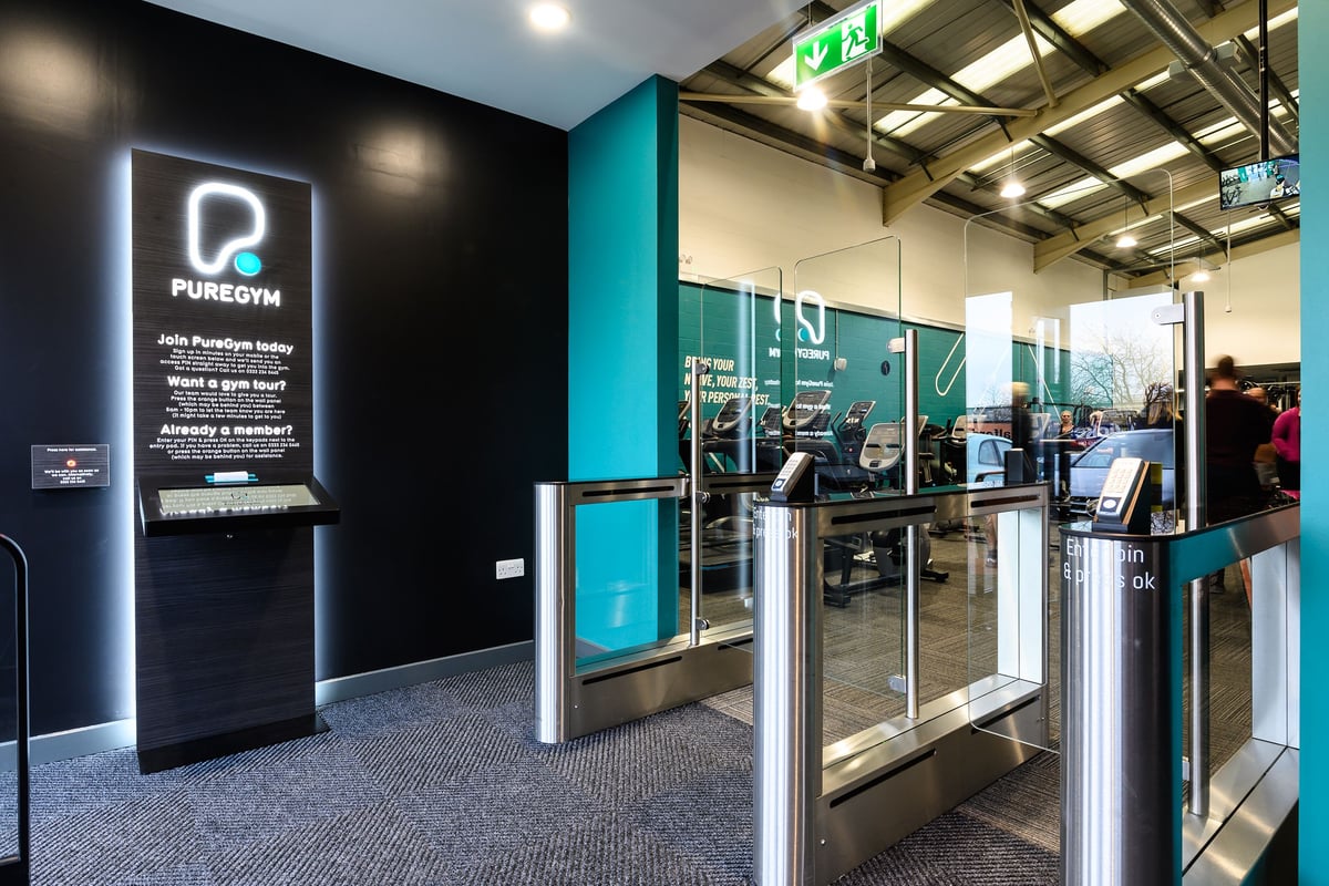 PureGym Burgess Hill: Entry area with turnstiles, neon signs and an exit sign.