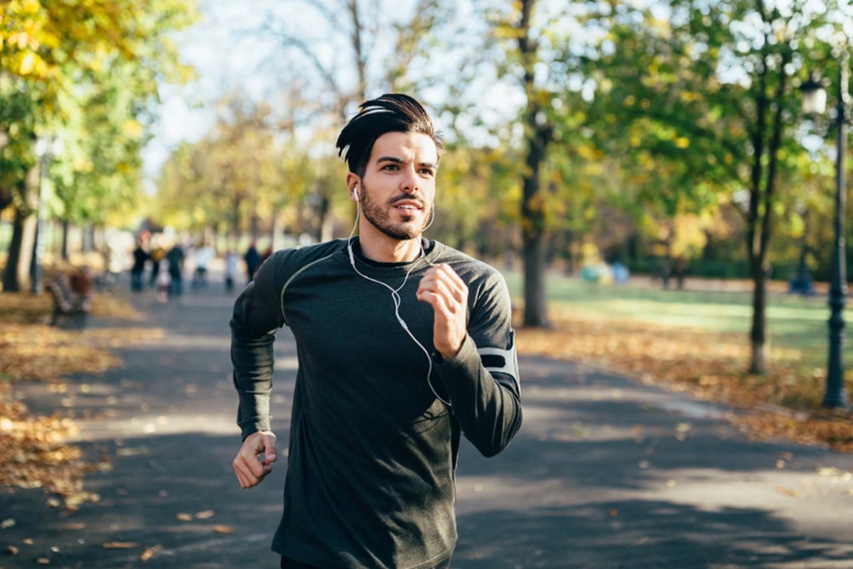 Man jogging in autumn park wearing earphones and a black long-sleeve shirt