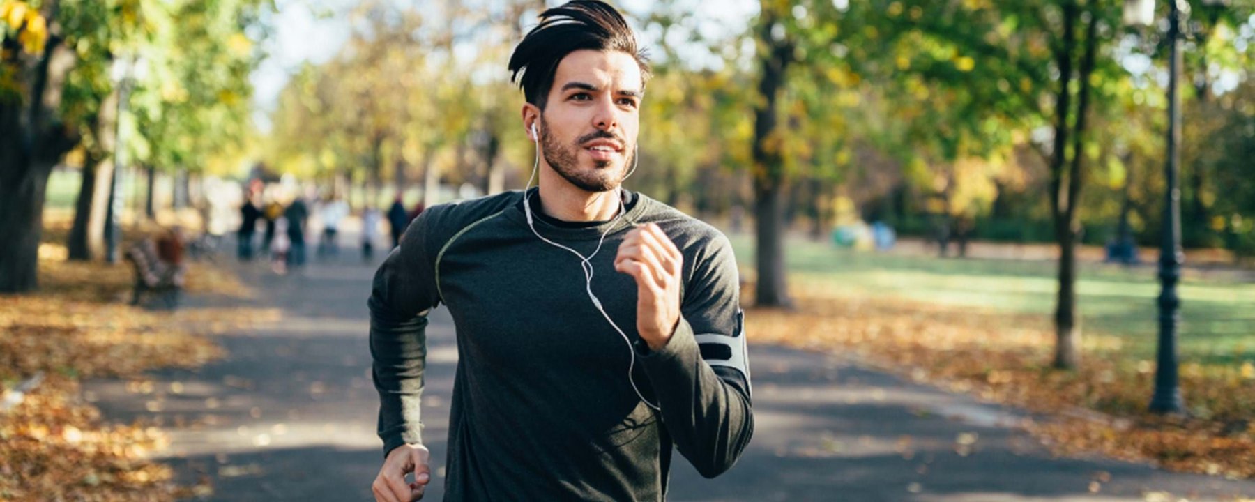 Man jogging in autumn park wearing earphones and a black long-sleeve shirt