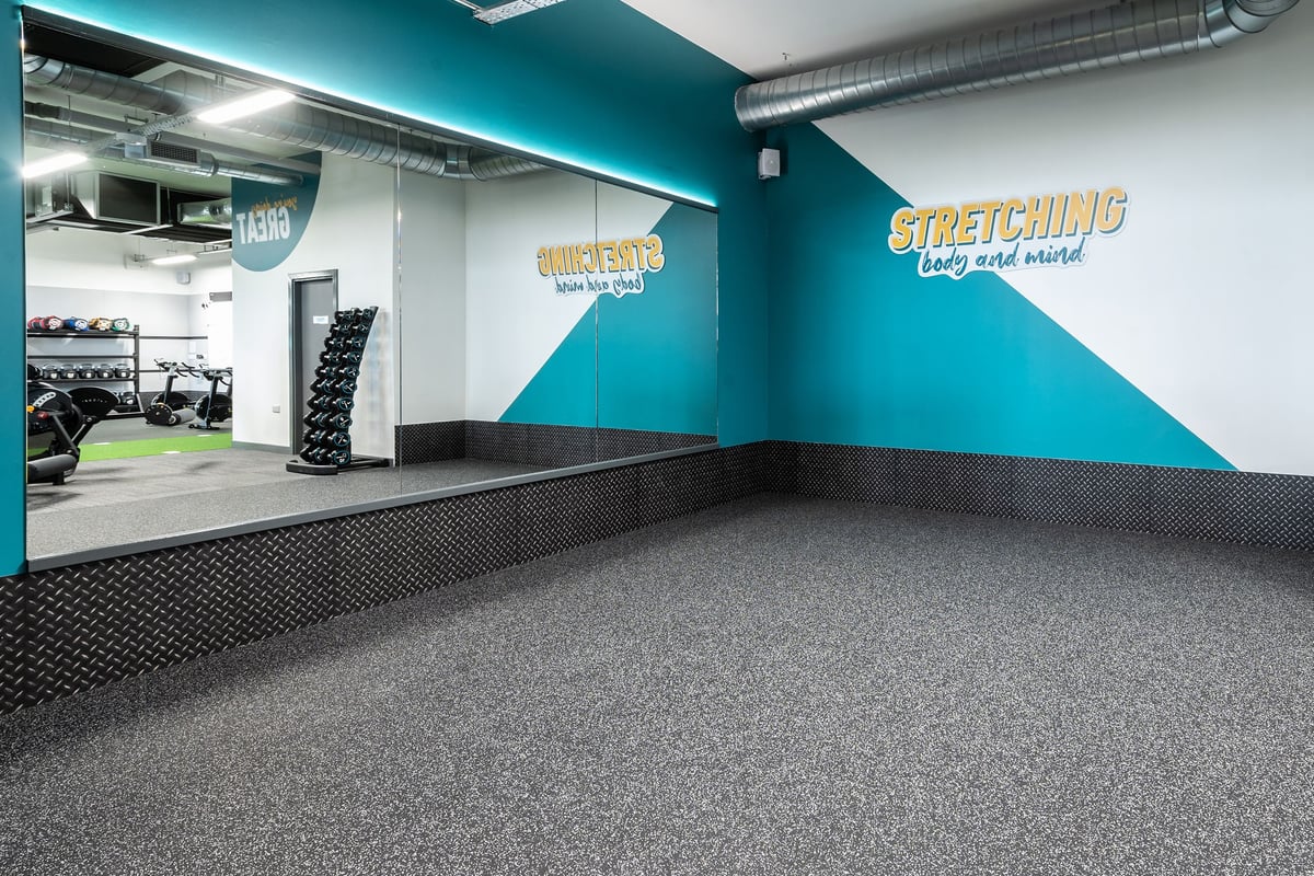 PureGym Nottingham West Bridgford: Stretching area with resistance machines, free weights, and teal accent wall.