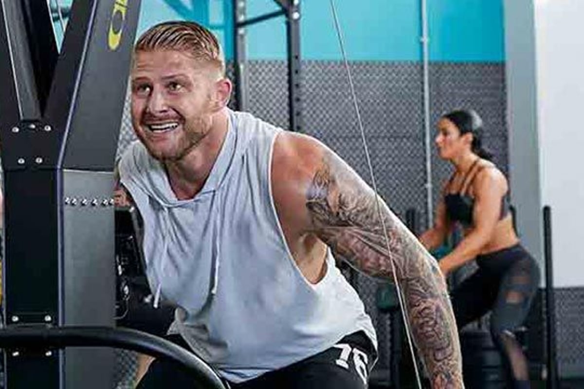 Homme au bras tatoué s’entraîne sur appareil de gym pendant que deux femmes font du sport