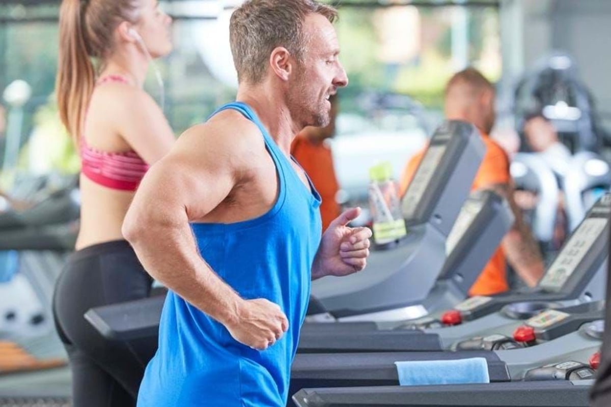 Man and woman running on treadmills in a gym with other people exercising nearby
