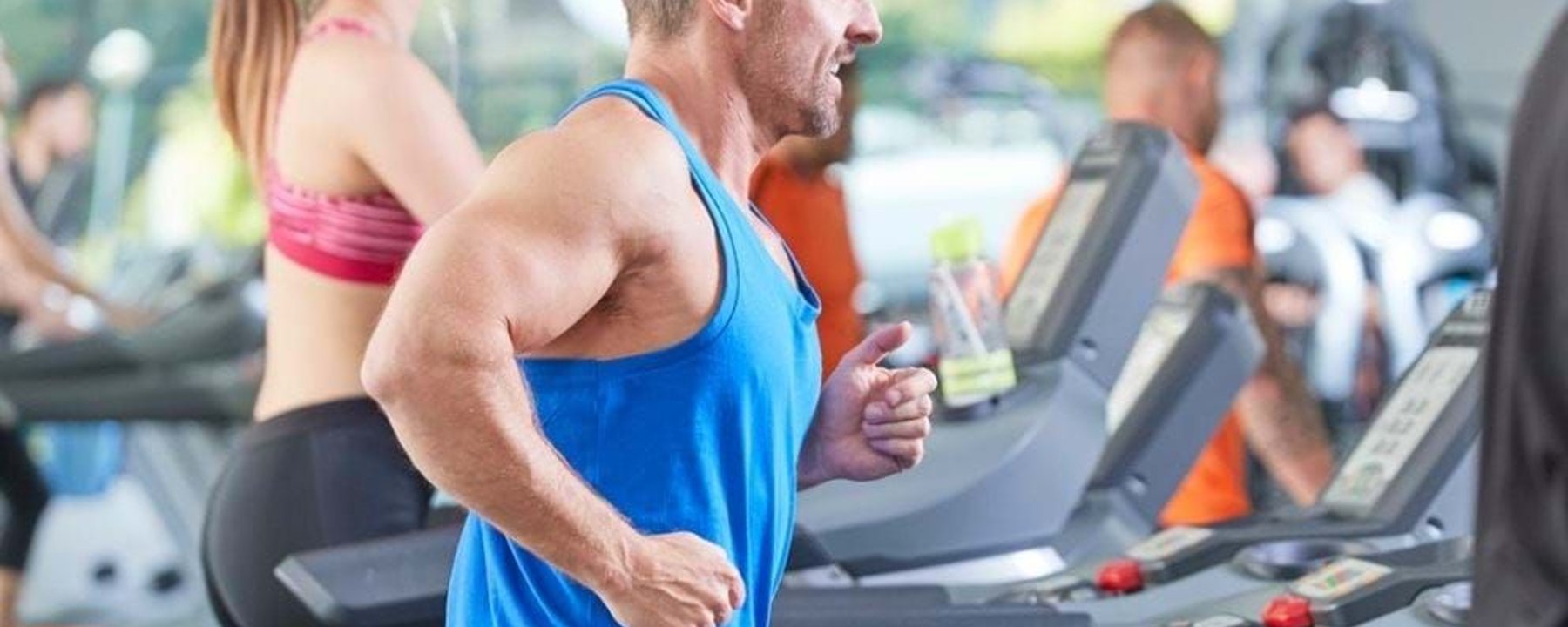 Man and woman running on treadmills in a gym with other people exercising nearby