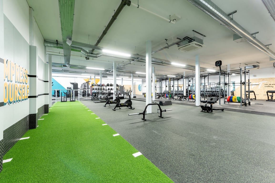 PureGym Peterborough Brotherhood Retail Park: Squat racks, weight plates, turf area, and free weights, in an open floor gym.
