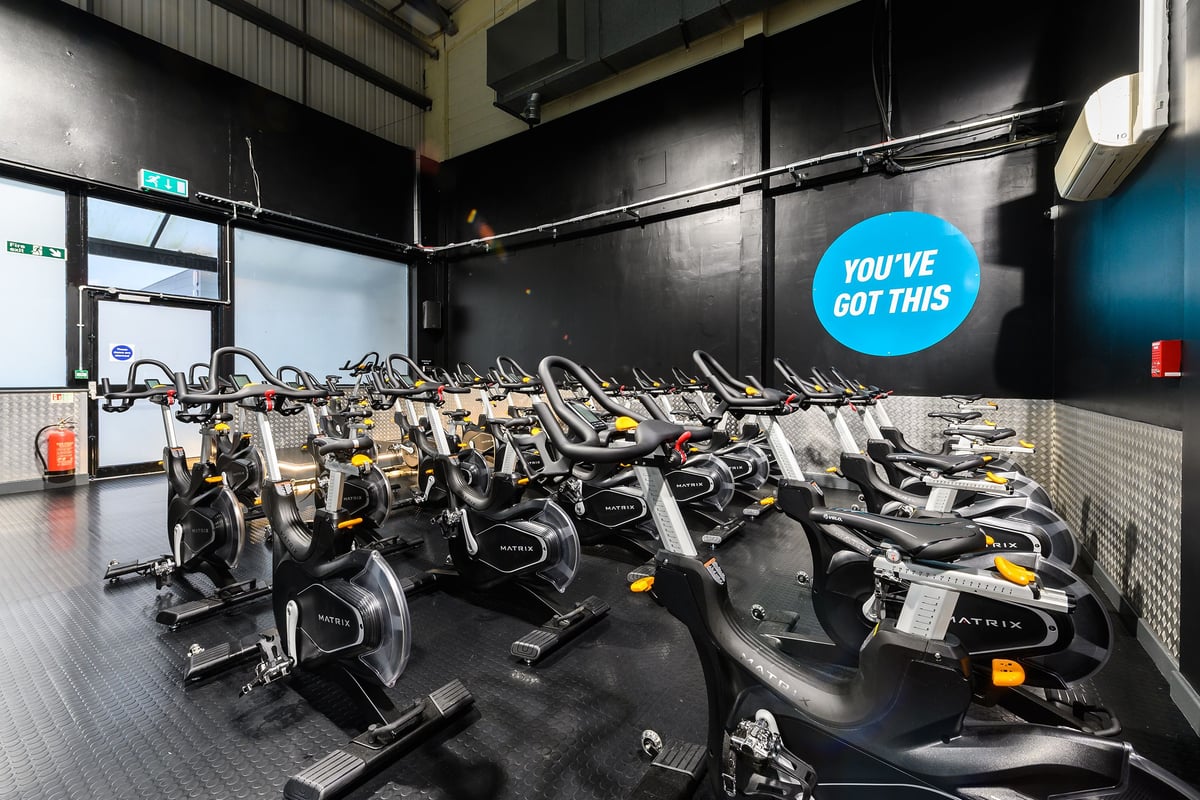 PureGym Bromborough: Rows of stationary exercise bikes in a dimly lit fitness studio interior.
