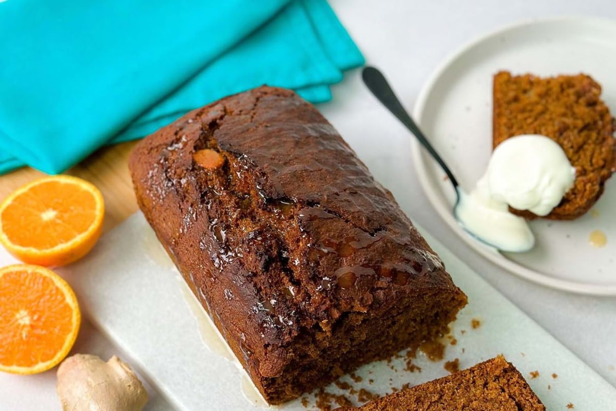 Loaf of gingerbread cake with a slice cut, orange halves, and a piece with cream on a plate