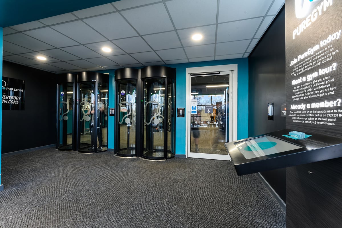 PureGym Nottingham Basford: Rows of futuristic fitness capsules, teal accents, black walls, floor mat.