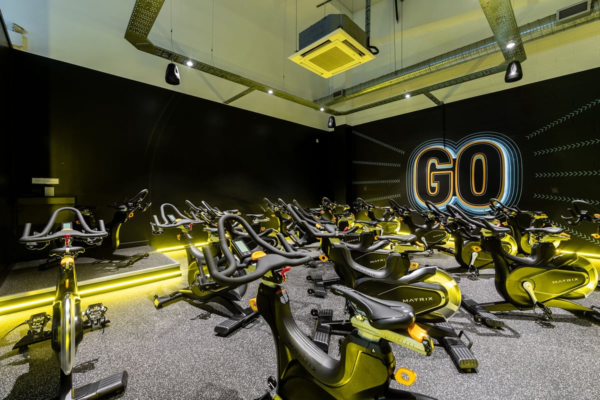 PureGym Banbury Cross Retail Park: Spin bikes arranged in rows with yellow lighting and a large "GO" sign on the wall.
