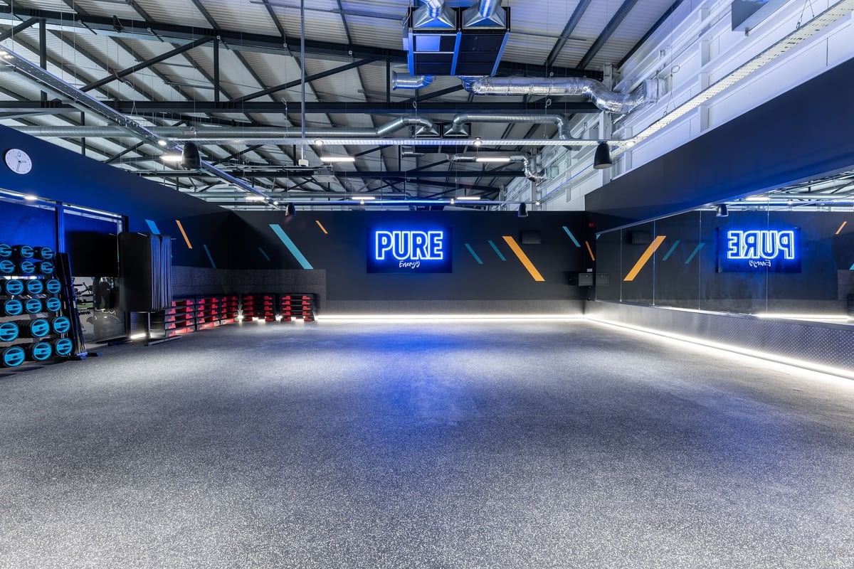 PureGym Ipswich Ravenswood: Weights area with benches, rubberized floor, suspended lighting, and blue branding displays.