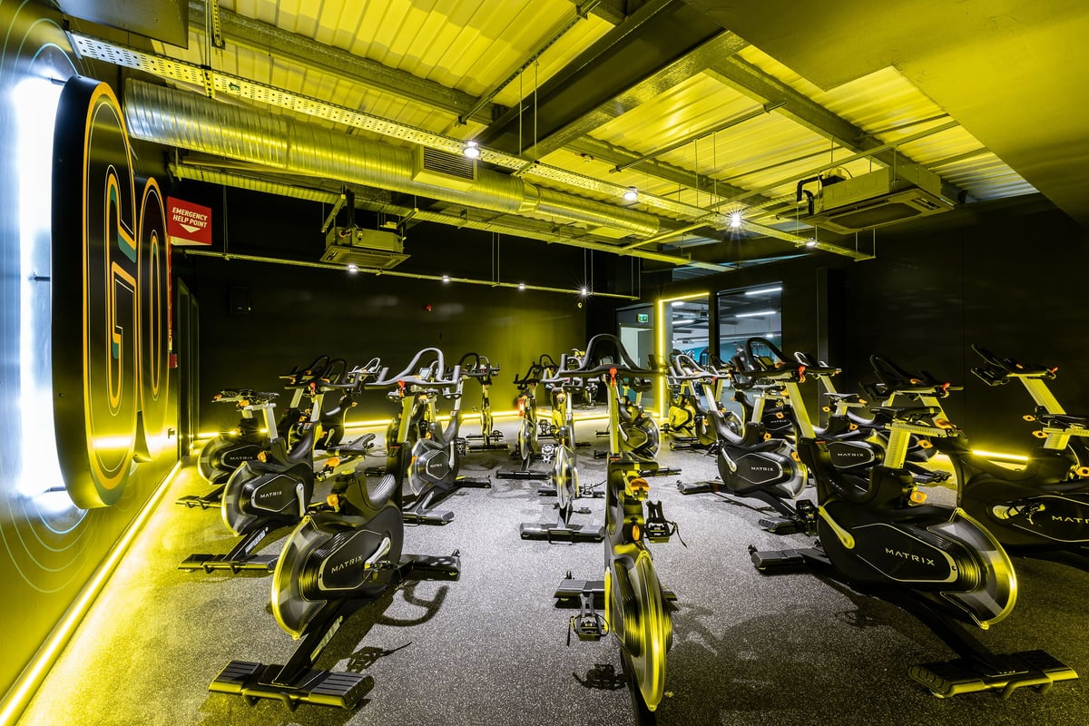 PureGym West Thurrock: Rows of stationary bikes, dimly lit by yellow neon lighting and ceiling lamps.