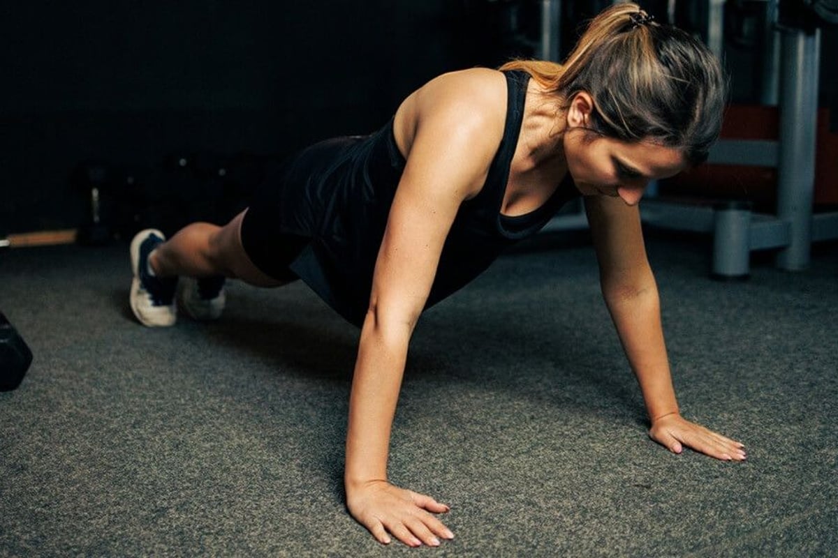 Woman in black workout clothes performing a press-up on a grey gym floor