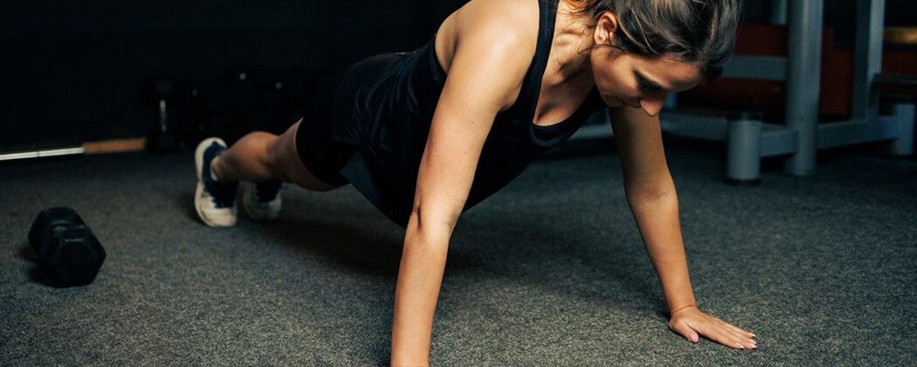 Woman in black workout clothes performing a press-up on a grey gym floor