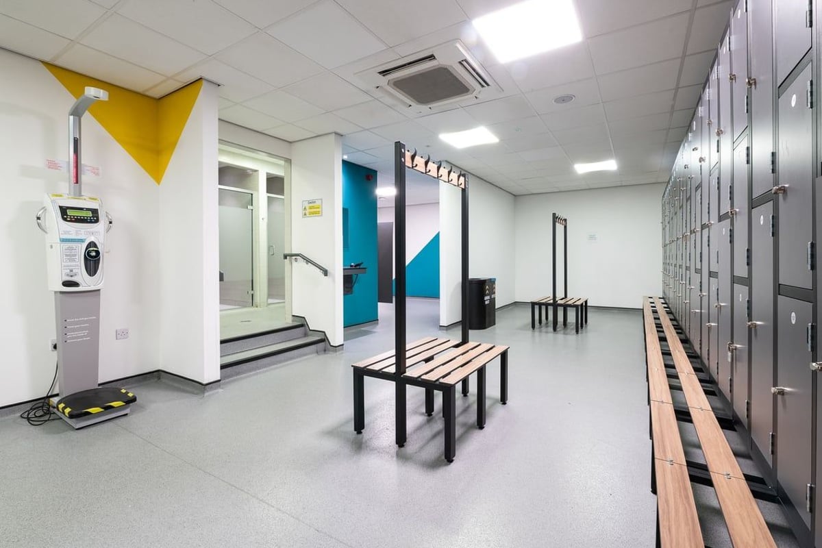 PureGym Leeds Bramley: Lockers, benches, colourful padded panels along mirrored walls - workout studio interior.