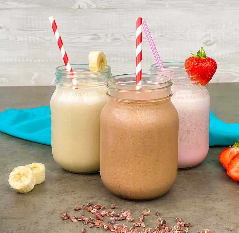 Three jars of milkshakes with striped straws, banana slices, and a strawberry garnish.