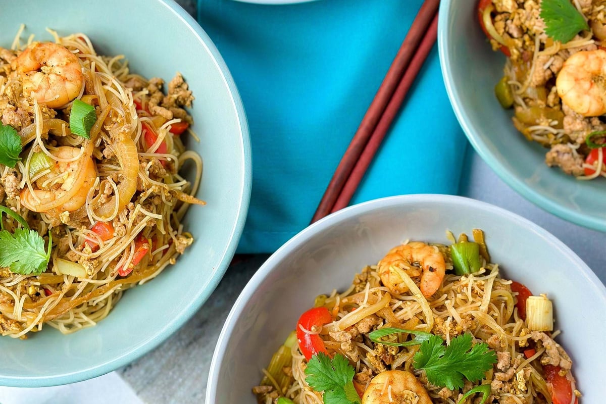 Four bowls of prawn and vegetable stir-fried noodles with chopsticks on a blue napkin
