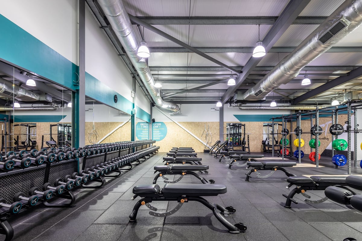 PureGym Cardiff Gate: Gym studio with weight machines, free weights, benches, rubberized flooring, and teal accent walls.