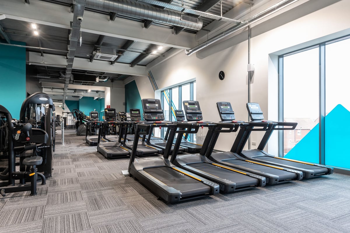 PureGym Bicester: Rows of treadmills, sleek design with turquoise accents and exposed ductwork.