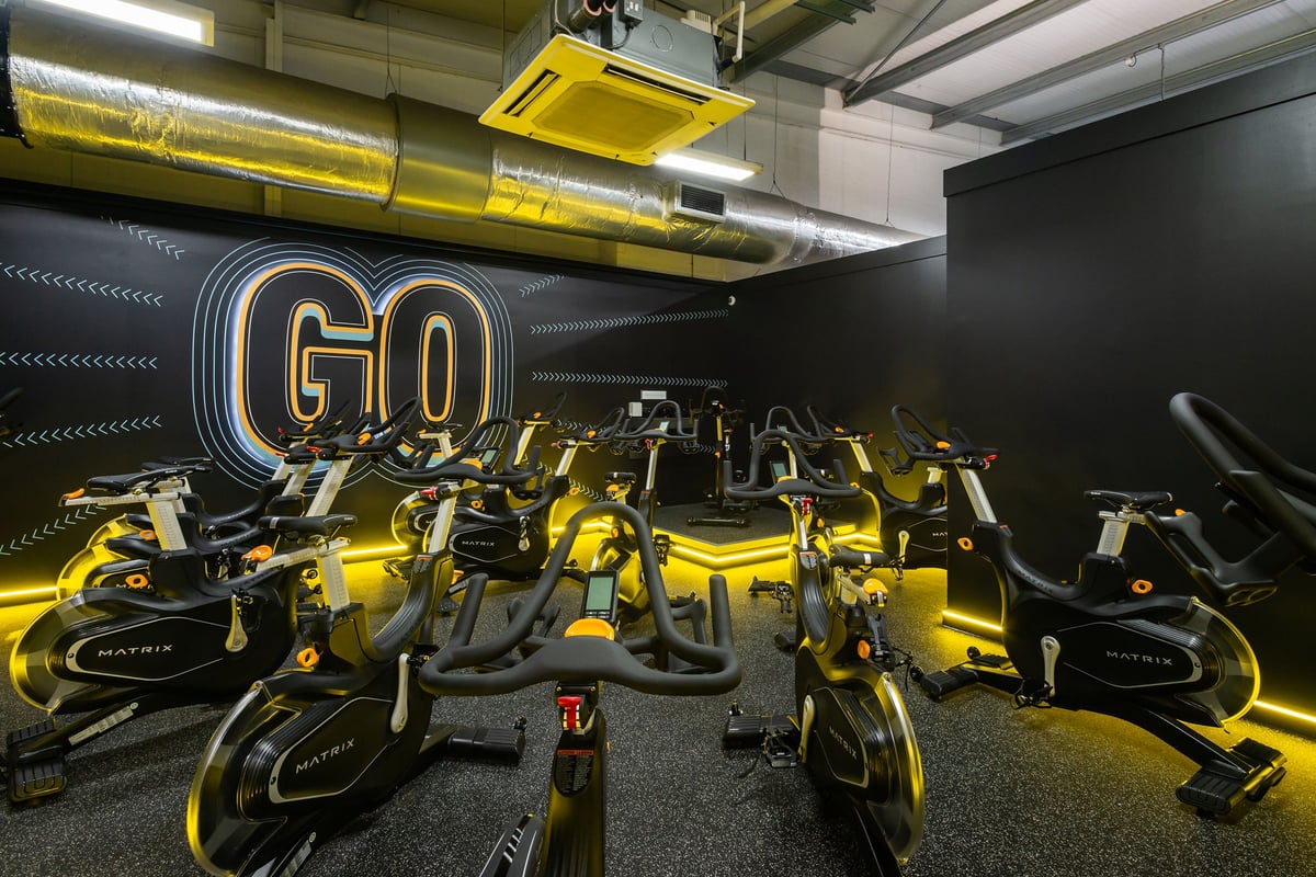 PureGym Wrexham: Rows of yellow stationary exercise cycles fill a dimly lit studio interior.