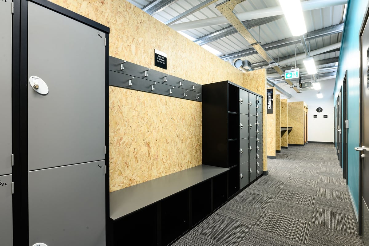 PureGym Rayleigh: Rows of lockers, benches in dimly lit corridors with rubberized flooring.