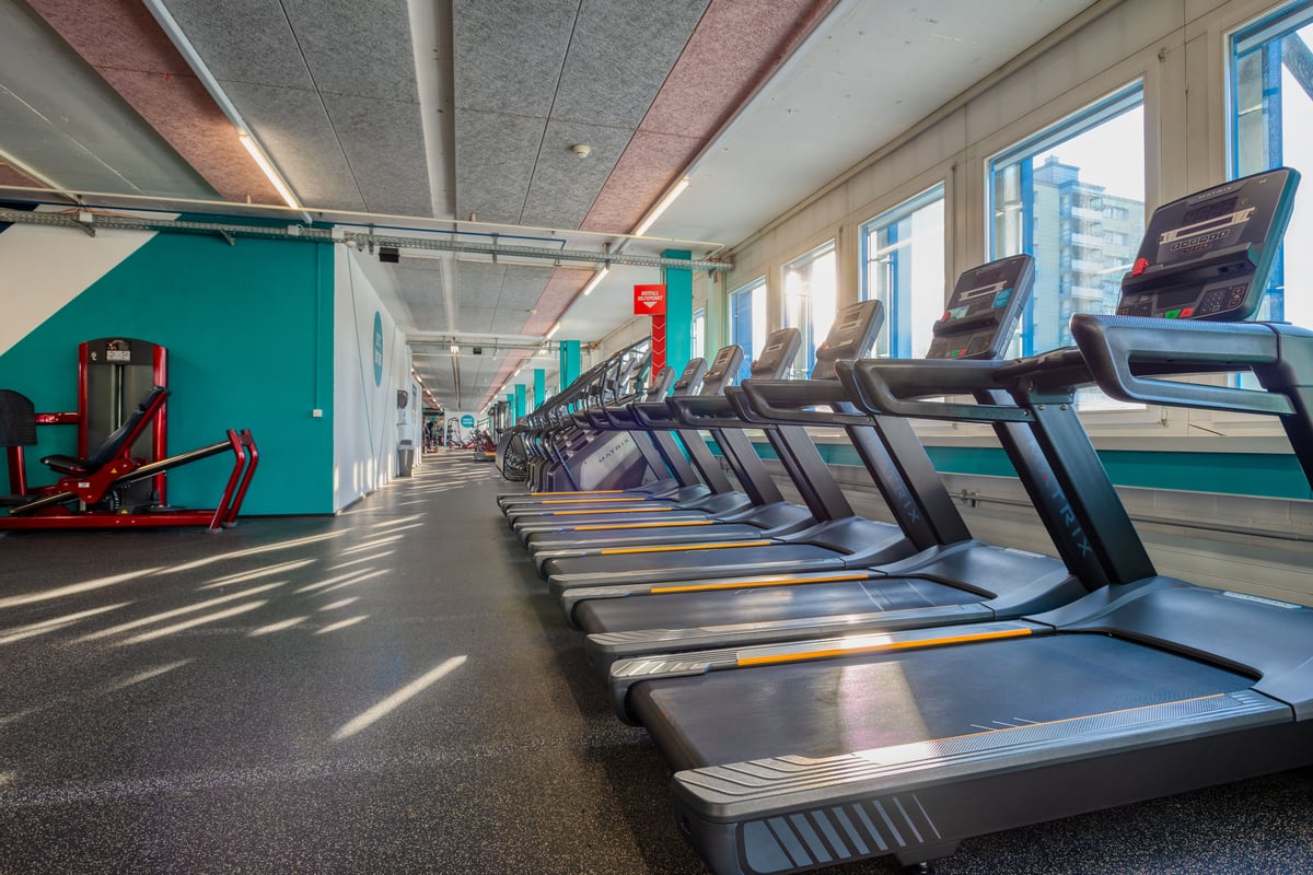 PureGym Wetzikon: Reihen von Laufbändern, Crosstrainern und Heimtrainern in einem hellen Fitnessstudio mit blaugrünen Akzentwänden.