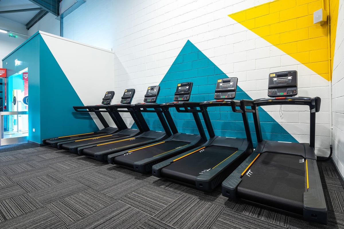 PureGym Linlithgow: Rows of treadmills in a bright space with teal and yellow accent walls.