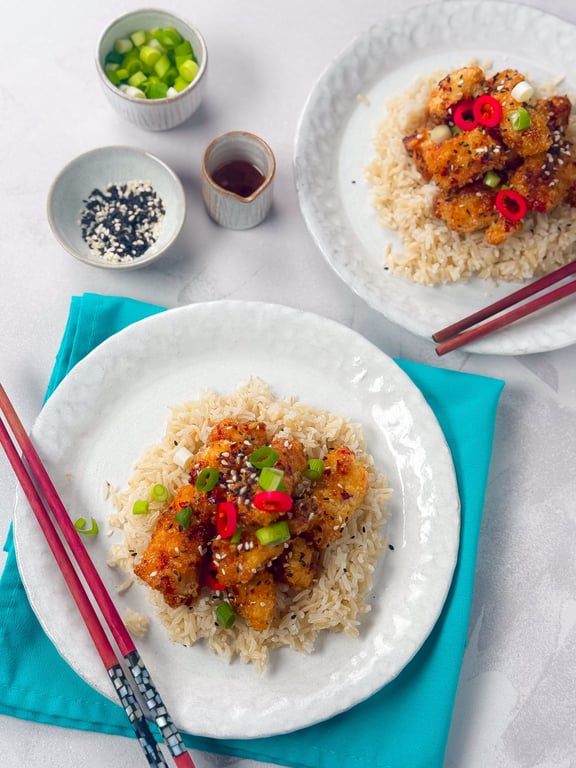 Two plates of crispy chicken with rice, garnished with spring onions and red chili slices