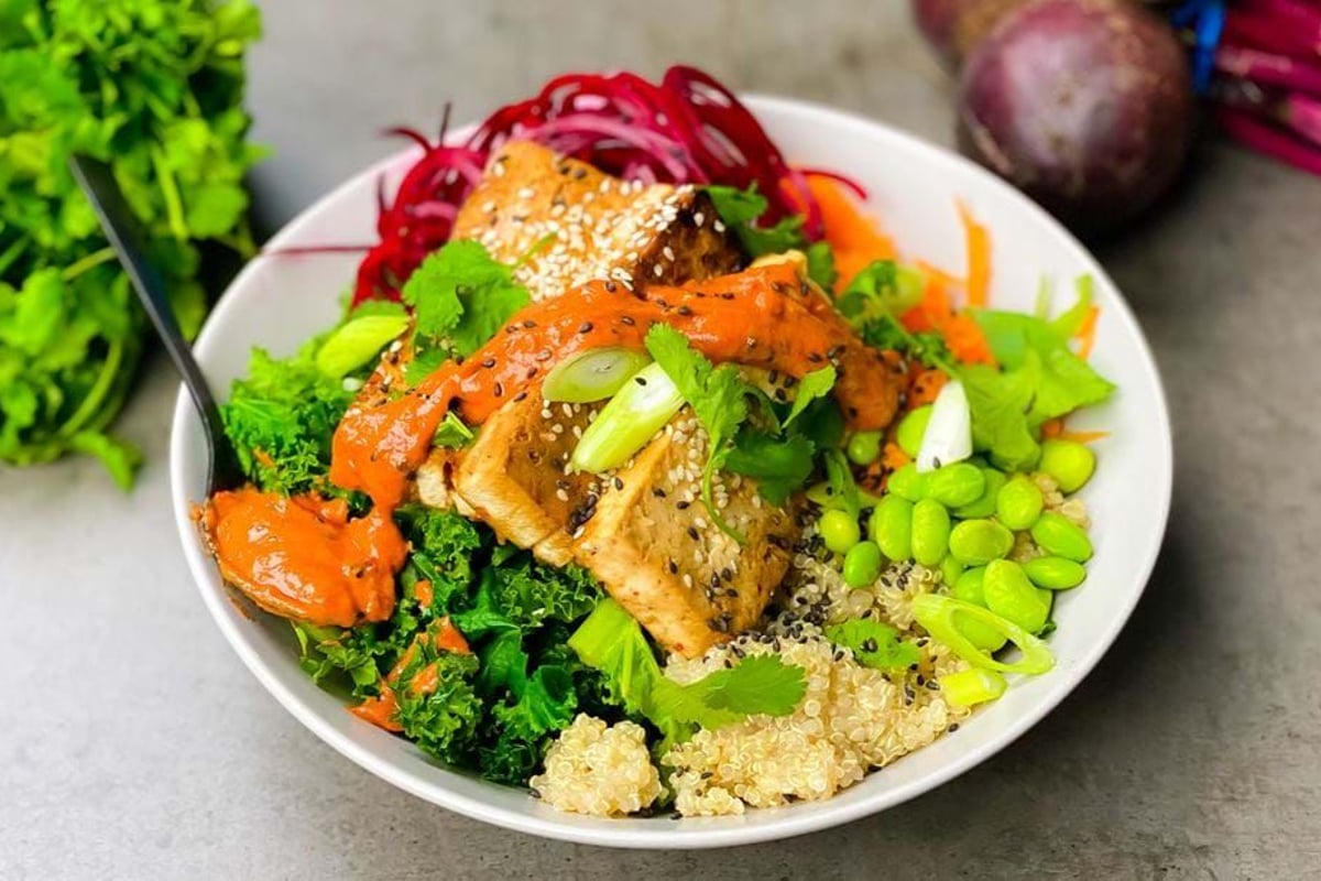 Bowl of tofu, quinoa, kale, edamame, shredded beetroot, carrot, and sauce.