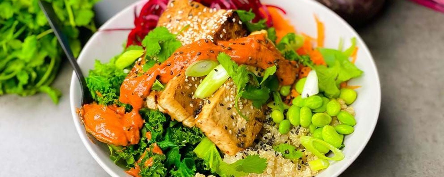 Bowl of tofu, quinoa, kale, edamame, shredded beetroot, carrot, and sauce.