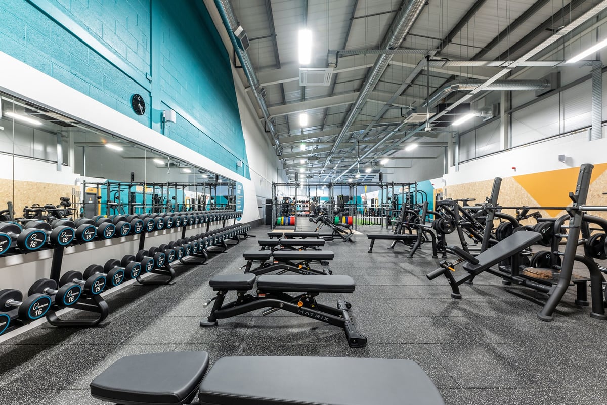 PureGym Byfleet: Rows of weight benches, dumbbells, weightlifting platforms, and rubberized floors in the gym.