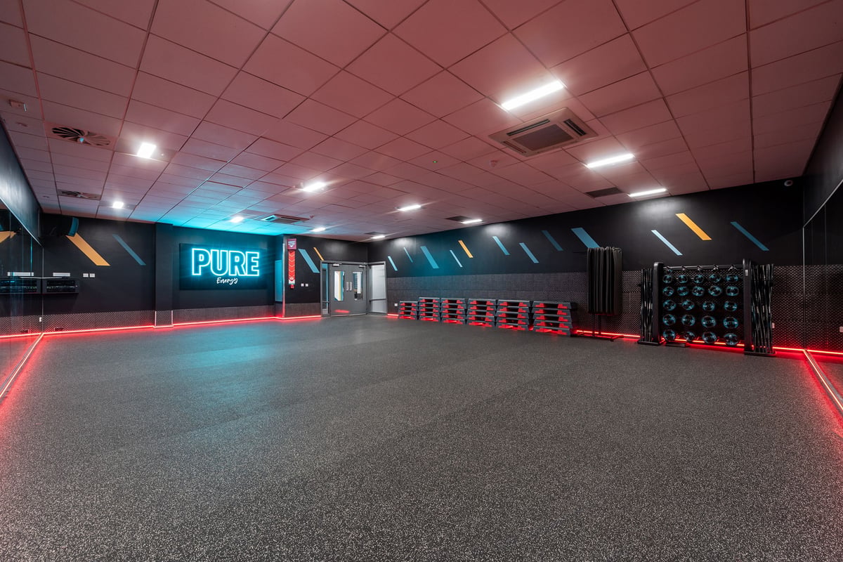 PureGym Loughborough: Teal and red lit corridor with Pure sign, lockers, and rubberized flooring.